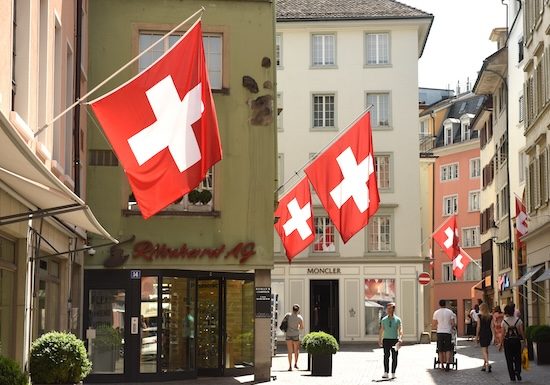 Zurich, Switzerland - June 03, 2017: People on the street of Zurich decorated with flags of Switzerland. Swiss Flags on the facade building in historic city center of Zurich, Switzerland @ credit Depositphotos