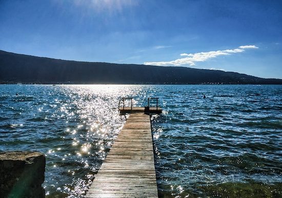 Lac d'Annecy, Menthon Saint Bernard, France - July 03, 2016: High contrast of the sun we see a jetty with people sitting on it, calm and enjoying the sun @ credit Depositphotos