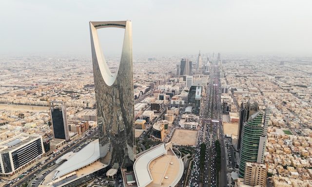 The drone gracefully soars over Riyadh, Saudi Arabia, capturing the majestic Kingdom Tower in the radiant daylight. Sunrise. The city sprawls beneath, reflecting modernity in its architecture, while the towering landmark stands as a beacon of progress. The image encapsulates Riyadh's vibrant spirit in the bright embrace of the sun. High quality 4k footage
