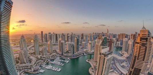Perspectives | Dubaï confronté à une chute historique de l’occupation hôtelière en 2026, selon Moody’s Sunrise over Dubai Marina skyscrapers and jumeirah lake towers panoramic view from the top aerial morning timelapse in the United Arab Emirates. Floating yachts and boats