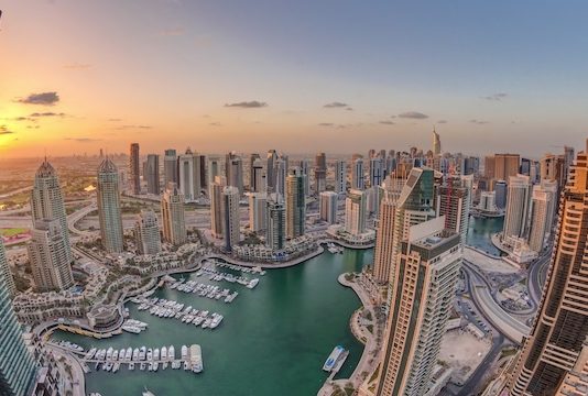 Perspectives | Dubaï confronté à une chute historique de l’occupation hôtelière en 2026, selon Moody’s Sunrise over Dubai Marina skyscrapers and jumeirah lake towers panoramic view from the top aerial morning timelapse in the United Arab Emirates. Floating yachts and boats