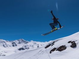Young female skier jumping from ski jump on sunny day in snowy alpine mountains, moment in flight.