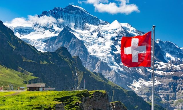 Swiss flag wavingon a Mannlichen viewpoint with peak of Jungfrau mountain on the background, Bernese Oberland Switzerland @ credit Depositphotos