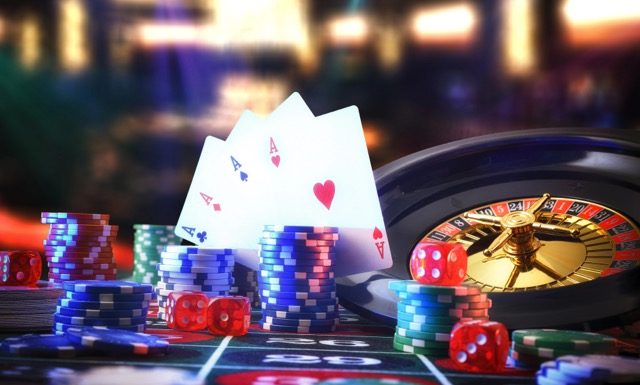 Detail of casino gaming table with game mat with stacks of betting chips on numbers and roulette, cards and dice with dark background of gaming room with lights. Front view.