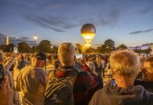 🇫🇷🥖🗼❤️ Baromètre du tourisme parisien | Un été stable : fréquentation touristique 2025 au niveau de 2023 Paris, France - 07 28 2025: People standing from behind take photos with cellphones of the Olympic Cauldron as it takes flight from the Tuileries Garden at sunset.