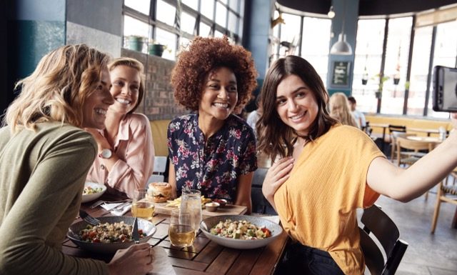 Four Young Female Friends Meeting For Drinks And Food Posing For Selfie In Restaurant