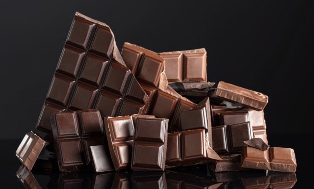 Broken bitter and milk chocolate bars on a black reflective background. Copy space.