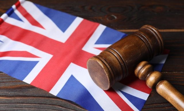 Judge's gavel and flag of United Kingdom on wooden table, closeup