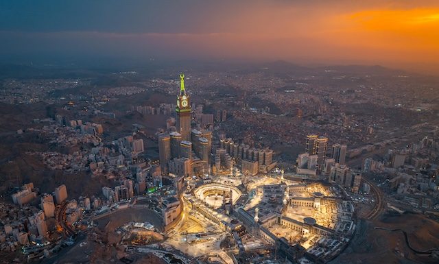Aerial view at night of the illuminated Grand Mosque and Abraj Al-Bait Clock Tower in Mecca, showcasing the city’s vibrant glow as lights shimmer across the holy site @ credit Depositphotos.com