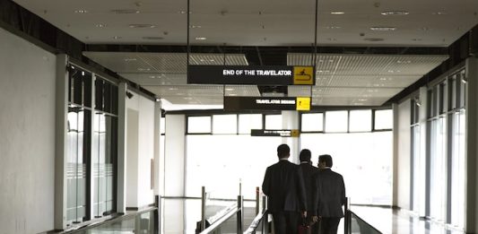 USA | Le voyage d’affaires aux États-Unis génère 623 milliards $ de PIB en 2024 businessmen walking on an airport moving walkway, discussing strategy during a business trip. Professional corporate travel and partnership concept
