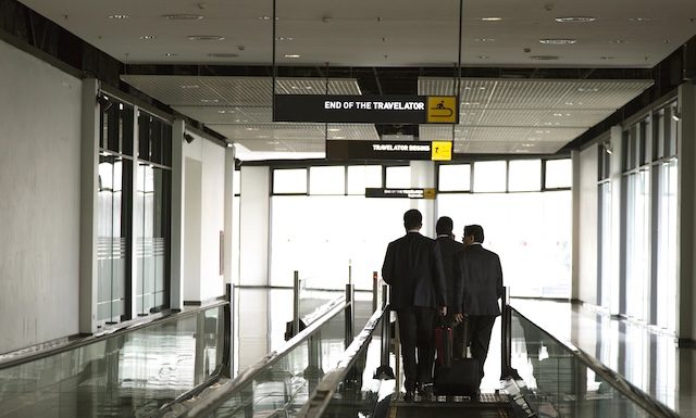 businessmen walking on an airport moving walkway, discussing strategy during a business trip. Professional corporate travel and partnership concept