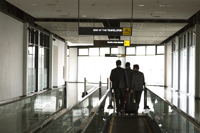 businessmen walking on an airport moving walkway, discussing strategy during a business trip. Professional corporate travel and partnership concept