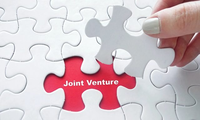 Close up of girl's hand placing the last jigsaw puzzle piece with Joint Venture