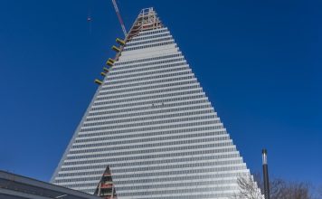 Paris, France - 02 26 2026: Porte de Versailles. Graphical view of two rappelling descent cleaners on The Triangle Tower building under construction and sunny blue sky