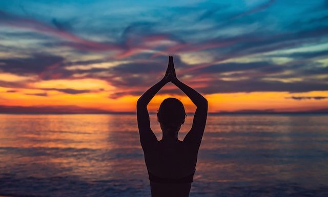 Young healthy woman practicing yoga on the beach at sunrise, benefits of natural environments for physical.
