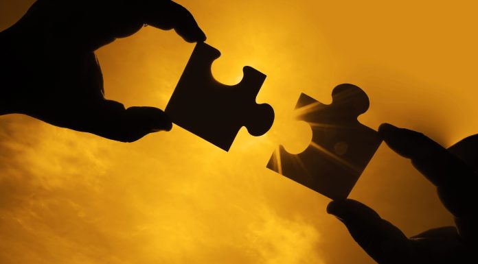 two hands trying to connect couple puzzle piece with sunset background. Jigsaw alone wooden puzzle against sun rays. one part of whole. symbol of association and connection. business strategy.