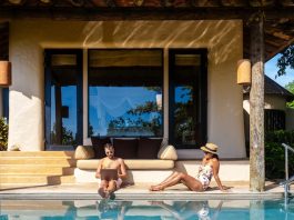 Strategy | Wyndham Rewards Expands into Holiday Rentals with Nearly 800 Homes and Villas Men working at a laptop a digital nomad working at a swimming pool during a vacation on a tropical island. man and woman in the infinity pool during sunset. luxury vacation in a luxury pool villa