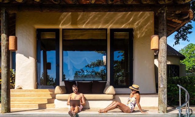 Men working at a laptop a digital nomad working at a swimming pool during a vacation on a tropical island. man and woman in the infinity pool during sunset. luxury vacation in a luxury pool villa