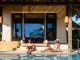Strategy | Wyndham Rewards Expands into Holiday Rentals with Nearly 800 Homes and Villas Men working at a laptop a digital nomad working at a swimming pool during a vacation on a tropical island. man and woman in the infinity pool during sunset. luxury vacation in a luxury pool villa